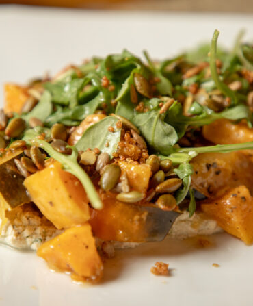 A close-up of roasted squash on a plate. The squash is on top of whipped mascarpone and has arugula and a brown dressing on top